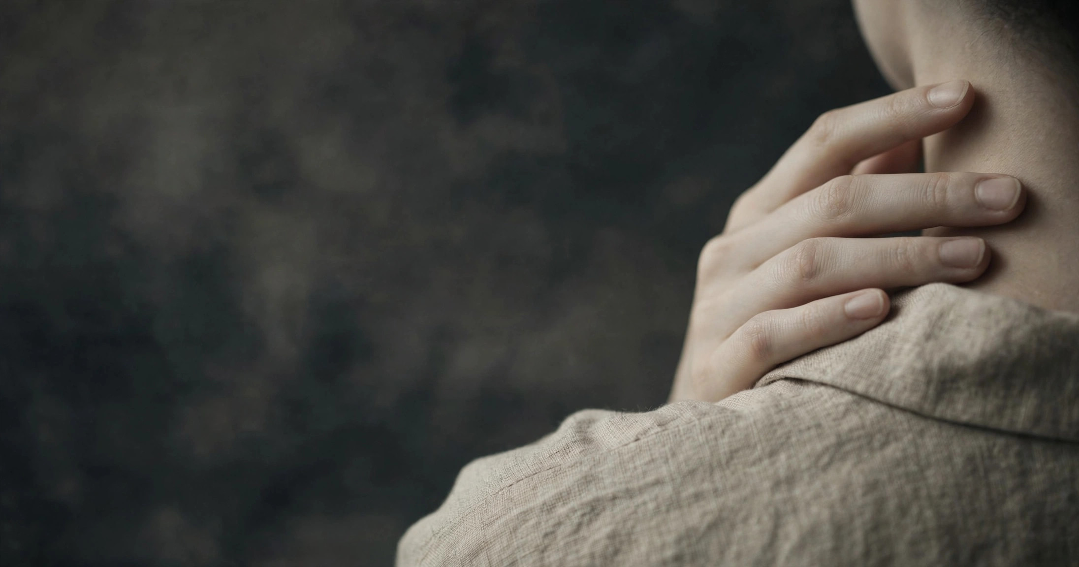 A hand gently touching the back of the neck and shoulder, in muted tones
